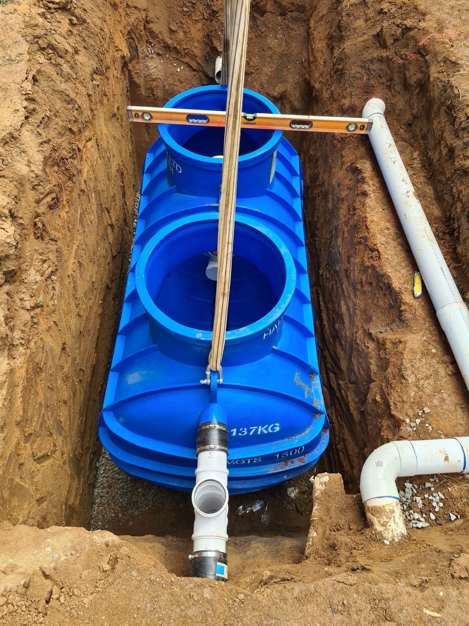Blue underground tank with PVC connections during installation.